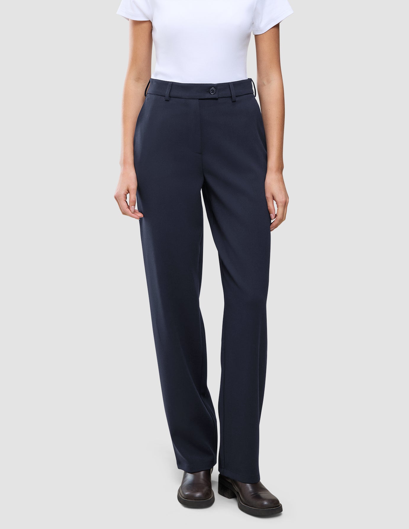 En person som har på seg en hvit T-skjorte stappet ned i Women GO2 Pants Straight Blue Nights og mørke skinnsko.